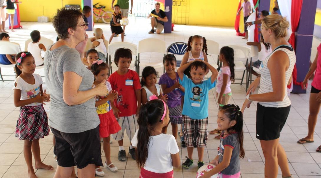Two Projects Abroad Childcare volunteers teach children how to play a game with a ball in Belize. A group of children are being taught how to play ball games by volunteers working with children in Belize.